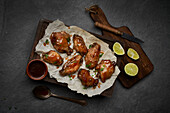 From above of appetizing grilled marinated chicken wings with ginger vinegar placed on plate with sauce and served with onions on wooden cutting board with knife on gray hard surface