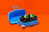 Horror lunch with black pasta and eyes in lunchbox placed on orange background
