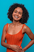 Smiling African American female model in casual clothes with dark curly hair looking at camera against blue background