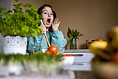 Portrait of cute surprised Caucasian girl in casuals with open mouth looking at camera while making salad at home
