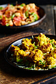 High angle of appetizing roasted cauliflower with green herbs served on black plate placed on wooden board against blurred traditional dish