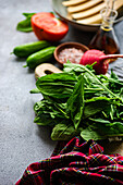 Lush Spinat Blätter Vorderseite auf einem Tisch mit geschnittenen Tomaten, Zucchini, und eine Schüssel mit Gewürzen, die alle für eine nahrhafte Salat Kreation vorbereitet