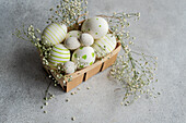 A charming collection of painted Easter eggs adorned with stripes and dots, nestled in a basket with delicate spring flowers