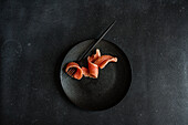Top view of healthy salmon slice served on black plate near fork against dark surface