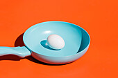 Ganzes rohes Ei auf blauer Keramikpfanne, isoliert vor leuchtend orangem Hintergrund