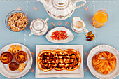 Eine Vielzahl gesunder Frühstücksprodukte, ordentlich auf einem blauen Tisch angerichtet, mit frischem Orangensaft und Tee