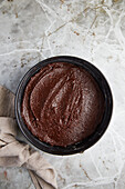 Top view of baking form filled with chocolate batter for cake near cloth on gray marble