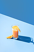 From above of squeezed orange juice garnished with orange slice on blue background