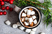 Draufsicht auf eine Tasse Kakao mit Marshmallow neben Tannenzweigen auf grauem Hintergrund in der Weihnachtszeit