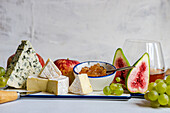 Assorted yummy snacks with different types of cheese and sweet served on ceramics plate with grapes apple and figs on table