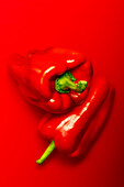 Top view of ripe red peppers placed on top of each other against red background