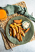 Top view of fried potato with paprika spice served with sour cream sauce on napkin with fork near napkin and orange juice against gray background