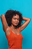 Portrait of slim African American female model in casual clothes with dark curly hair looking at camera against blue background