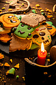 Draufsicht auf leckere Halloween-Kekse auf einem Teller auf einem Holztisch neben einem Seil mit einer brennenden Kerze