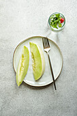 From above slices of green melon placed in a ceramic dish with a lemonade on concrete background
