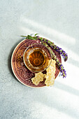 Draufsicht auf ein Glas Blumentee mit frischen Kräutern, serviert auf einem Keramikteller vor grauem Hintergrund