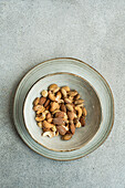 A selection of mixed nuts placed in a ceramic bowl, situated on a textured grey surface, offering a minimalist aesthetic
