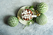 Top view of delicious cocoa with marshmallow on plate with fir twigs placed near Christmas balls