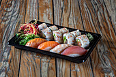 Black plastic container to go with sets of uramaki tuna sushi rolls and nigiri sushi with assorted fish together with seaweed salad