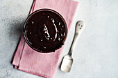 Top view of hot chocolate served in transparent glass with spoon on napkin against blurred background