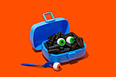 Horror lunch with black pasta and eyes in lunchbox placed on orange background near fork with eye