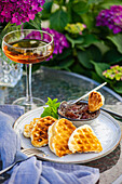 Blick von oben auf appetitliche süße Waffeln mit Pfirsichmarmelade auf rundem Tisch neben Glas mit Getränk im Garten mit blühenden lila Hortensienblüten