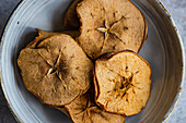 Top view of slices of dried apples served in ceramic bowl against blurred gray background