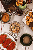 Cozy breakfast spread with pastries, granola, coffee, and tomato toasts on a patterned tablecloth.