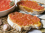 Close up of pieces of bread with tomato spread placed on table near bowl with tomato spread and garlic
