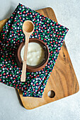 Draufsicht auf eine traditionelle Portion georgischen sauren Joghurts, bekannt als Matsoni, in einem Tontopf mit Holzlöffel auf einer bunten Serviette auf einem Holztablett vor einem unscharfen Hintergrund