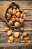 Almonds escape from a burlap bag, scattering on a weathered wooden table, capturing a sense of harvest abundance.