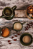 Ansicht von oben auf ein gemütliches Teearrangement mit zwei Tassen Tee, einer grünen Teekanne, Gewürzen und getrockneten Früchten auf einem rustikalen Holztisch