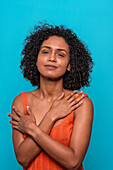 Smiling African American female model in casual clothes with dark curly hair and crossed arms looking at camera against blue background
