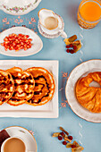 An array of breakfast foods spread out, featuring waffles, fruits, and beverages, on a vibrant blue background.