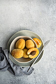 Draufsicht auf eine Keramikschale mit frischen reifen gelben Aprikosen auf blauem Tuch auf einem Betontisch mit halbierter Aprikose