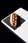 High angle of appetizing bun with sausage and ketchup with greens served table mat over white wooden board against black background in studio