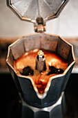 Nahaufnahme von blubberndem Kaffee in einer offenen Espressomaschine, die das reiche Aroma und die Konsistenz von frisch gebrühtem italienischen Kaffee in einer gemütlichen Umgebung einfängt