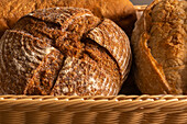 Focused of various tasty freshly baked pastry breads being served with baking pan into wicker basket with fabric on dining table indoors