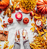 Autumn skin care Â´beauty products. Women hand holding cosmetic bottles at white background with fall leaves, candles, pumpkins and hot chocolate. Top view with copy space. Beauty lifestyle