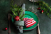 Kleine Weihnachtstüte und in Taschentuch gewickelte Tannenzweige auf Teller auf grünem Tisch neben Glas und Gabeln