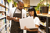 Serious multiethnic colleagues in aprons surfing laptop together while working in contemporary store and checking information during work process