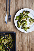 From above baked cooked green broccoli stems with cheese and pepper placed on wooden background near cutlery