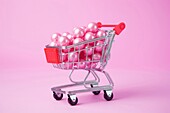 Komposition von Miniatur-Einkaufswagen mit verschiedenen bunten Mockup-Produkte auf rosa Hintergrund platziert