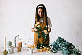 Concentrated female floral designer in apron standing at table and creating floral composition with blooming roses in workshop