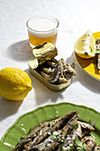 Von oben köstliche gebratene Sardellen auf Tellern mit Zitrone serviert und auf einem weißen Tisch mit einem Glas Bier platziert