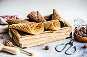 Wooden box with empty waffle cones, bowl with hazelnuts and tools for ice cream cooking