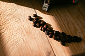 Hochformatige Aufnahme von frisch gerösteten Kaffeebohnen auf einem rauen Holztisch mit Kratzern in einer Küche im Sonnenlicht