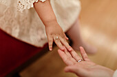 High angle of unrecognizable little girl in white lace dress with elegant ring on finger touching hand of anonymous bride