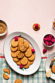 Top view of plates with delicious crispy homemade cookies and fresh raspberries served on table with teapot bowl of seeds