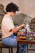Side view of focused female florist making flower wreath with ribbon bow while working in floral shop